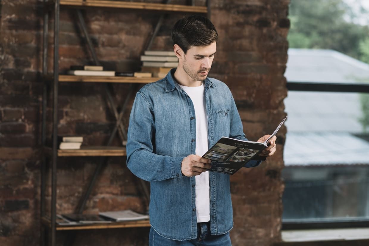 handsome-young-man-reading-magazine-standing-front-book-shelf
